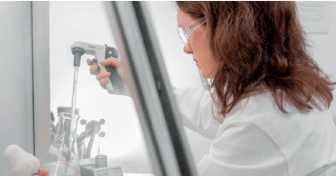 A lab technician using a device to mix liquid in a beaker.